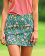 A woman wearing a pink golf polo and a green floral golf skort.