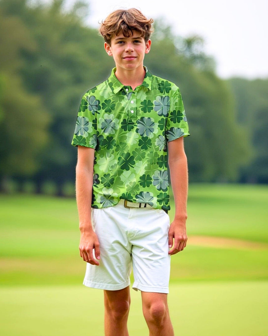 A young man stands on a golf course wearing a green polo shirt with a clover pattern and white shorts.