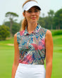 A woman wearing a sleeveless golf polo with a tropical leaf print and a white visor stands on a golf course.