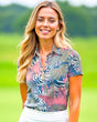 A woman smiles wearing a floral golf polo and white skirt on a golf course.