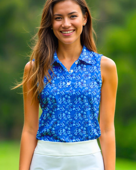A smiling woman in a sleeveless blue floral golf polo and white golf skirt stands on a golf course.
