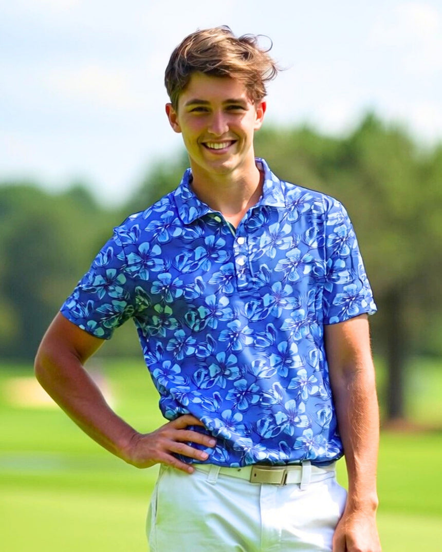 A smiling man in a blue floral golf polo stands on a golf course.