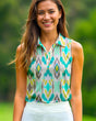A smiling woman in a sleeveless golf polo with a geometric pattern of teal, yellow, and gray diamonds, paired with a white golf skirt.
