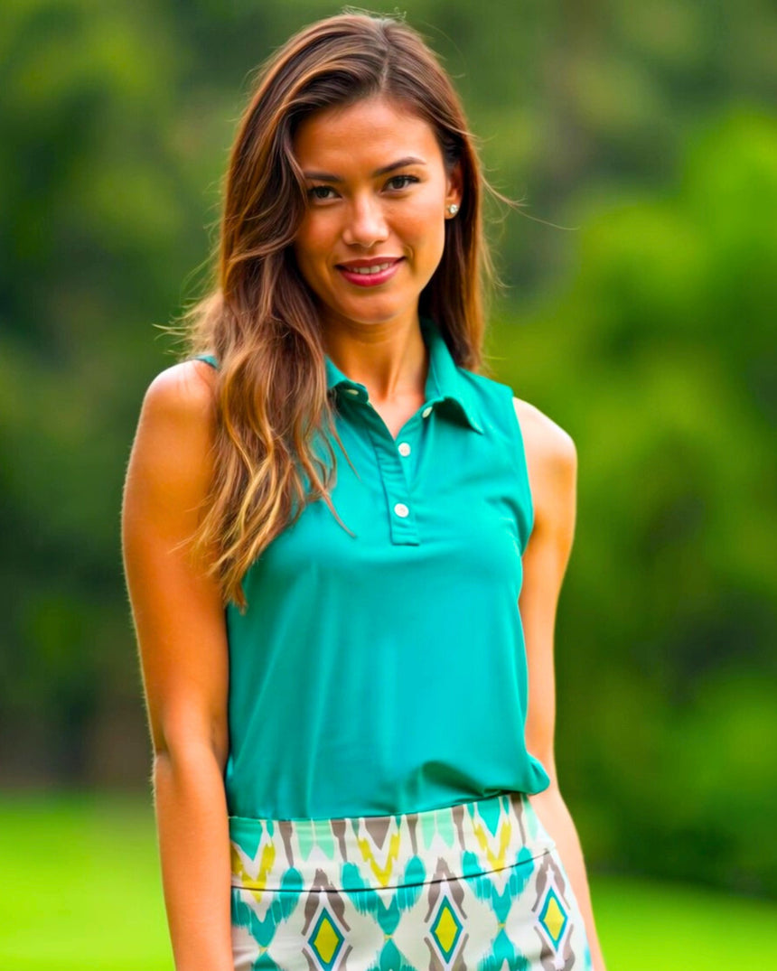 A woman smiles wearing a sleeveless turquoise golf polo and patterned golf skirt.