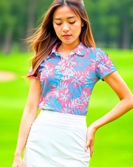 A woman in a pink and blue floral golf polo and white skirt stands on a golf course.