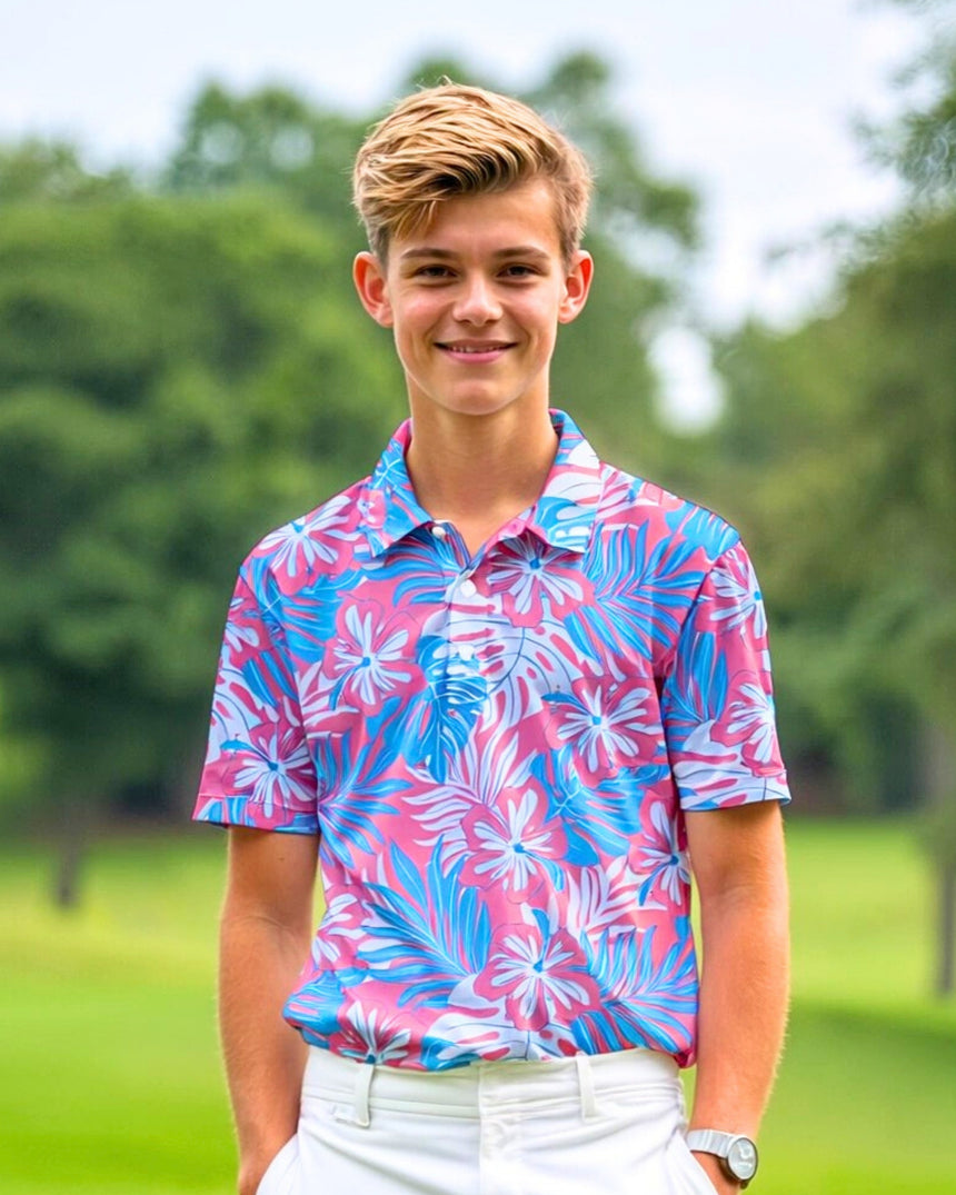 A young man smiles wearing a pink and blue floral golf polo shirt and white pants.