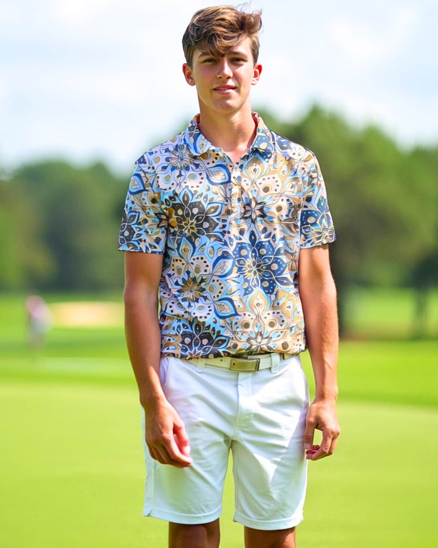 A young man stands on a golf course, wearing a patterned golf polo and white shorts.