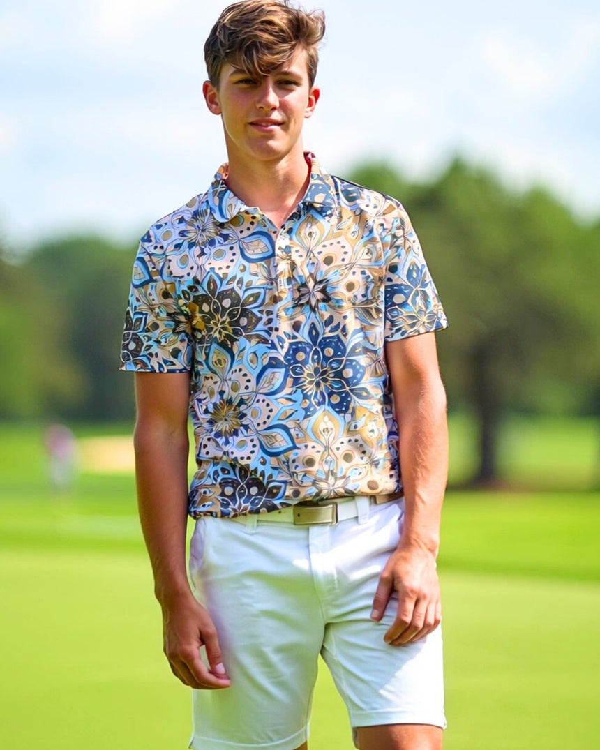 A young man stands on a golf course wearing a patterned golf polo, white shorts, and a belt.