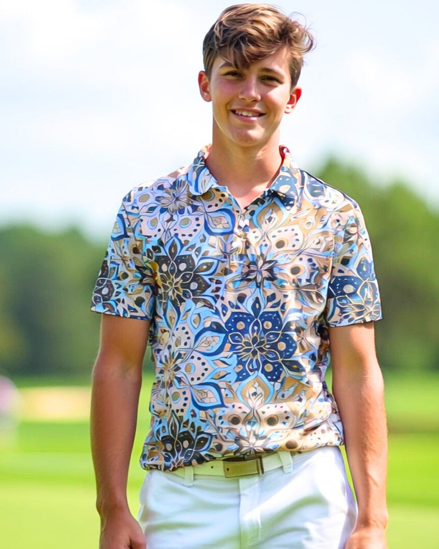 A young man smiles while wearing a patterned golf polo, white pants, and a white belt on a golf course.