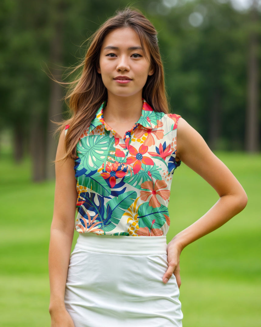 A woman stands on a golf course, wearing a white golf skirt and a sleeveless golf polo with a tropical floral pattern.