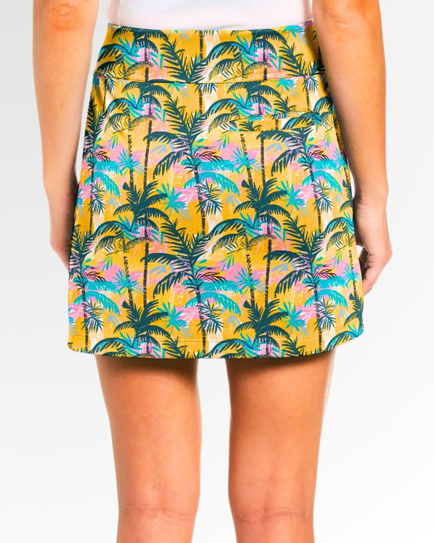Close-up back view of a woman wearing a golf skort with a yellow background and a pattern of green and blue palm trees.
