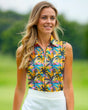 A woman smiles wearing a sleeveless golf polo with a colorful palm tree pattern and a white skirt on a golf course.