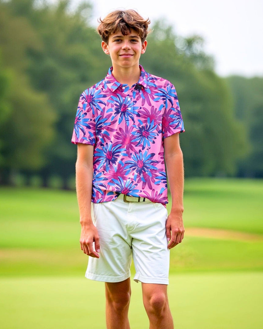A young man stands on a golf course, wearing a pink golf polo with a blue and purple floral pattern, paired with white shorts.