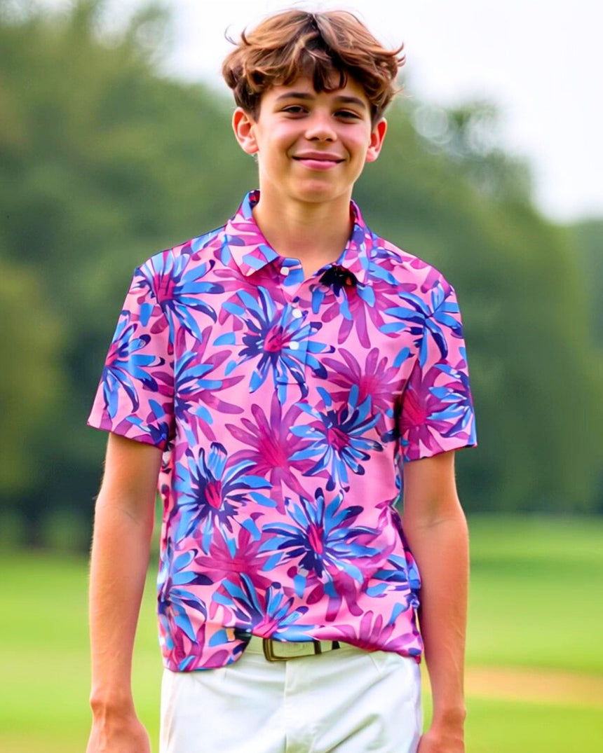 A young man smiles wearing a pink golf polo with blue and purple flowers, paired with white golf pants.