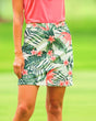 A woman wearing a pink golf polo and a white golf skirt with a tropical floral and leaf pattern.