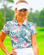 A woman in a white visor and a tropical print golf polo stands on a golf course.