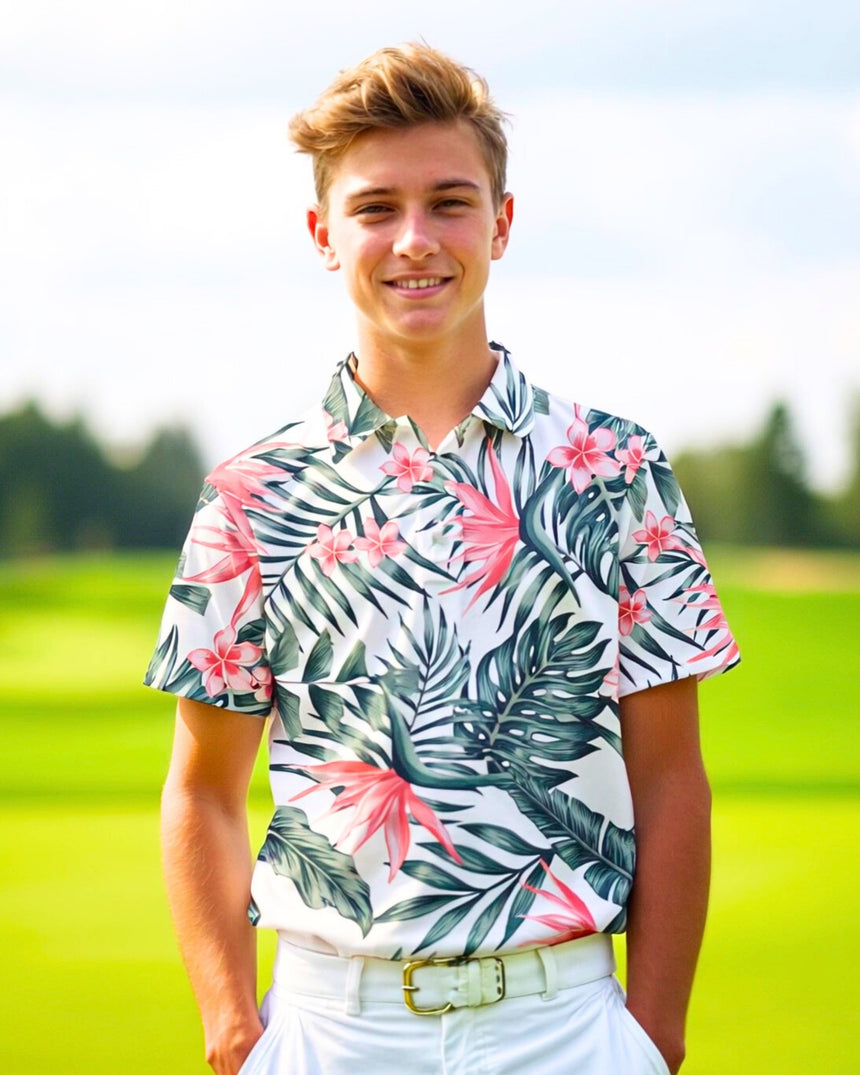 A smiling young man in a floral golf polo and white pants stands on a golf course.