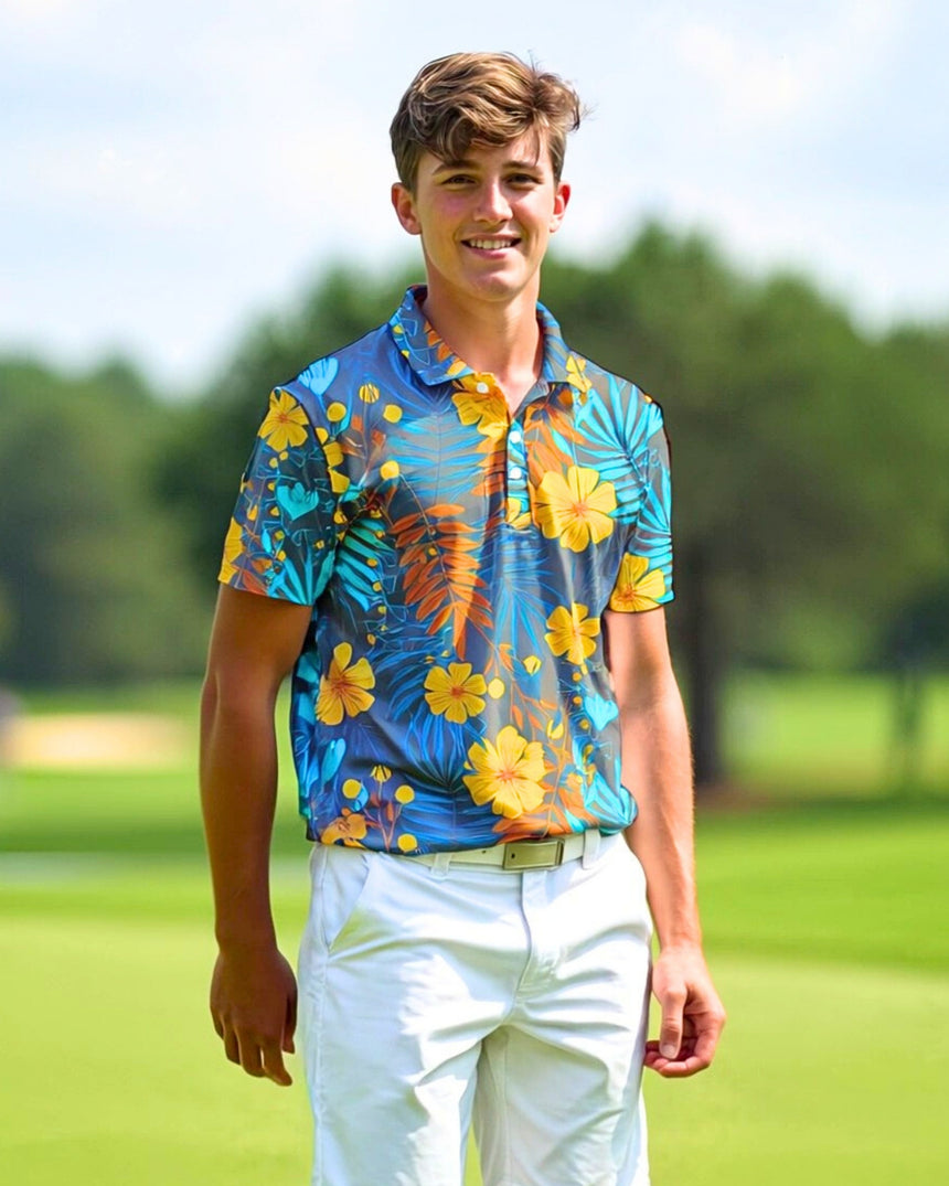 A young man smiles while wearing a blue, yellow, and orange floral golf polo and white pants on a golf course.