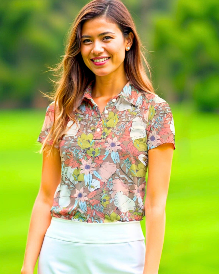 A smiling woman in a floral golf polo and white skirt stands on a golf course.