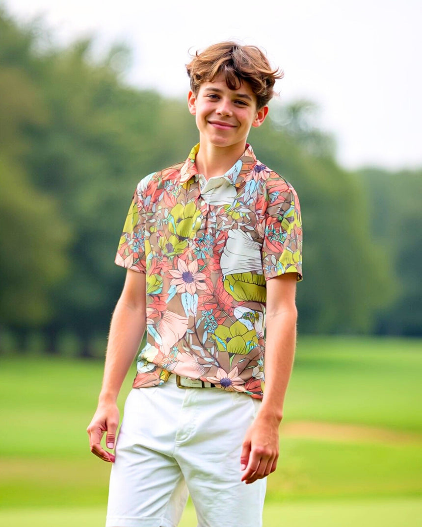A young man smiles, wearing a floral golf polo and white shorts on a golf course.