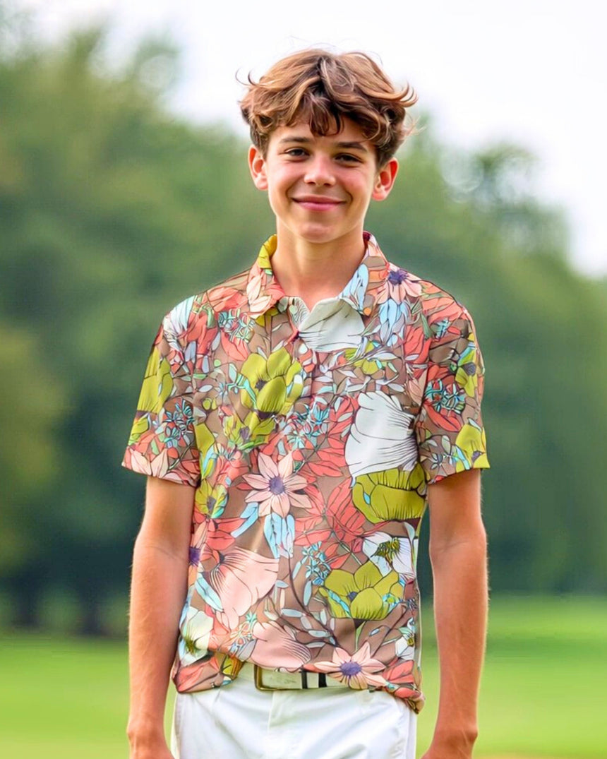 A smiling young man stands on a golf course wearing a floral golf polo and white pants.
