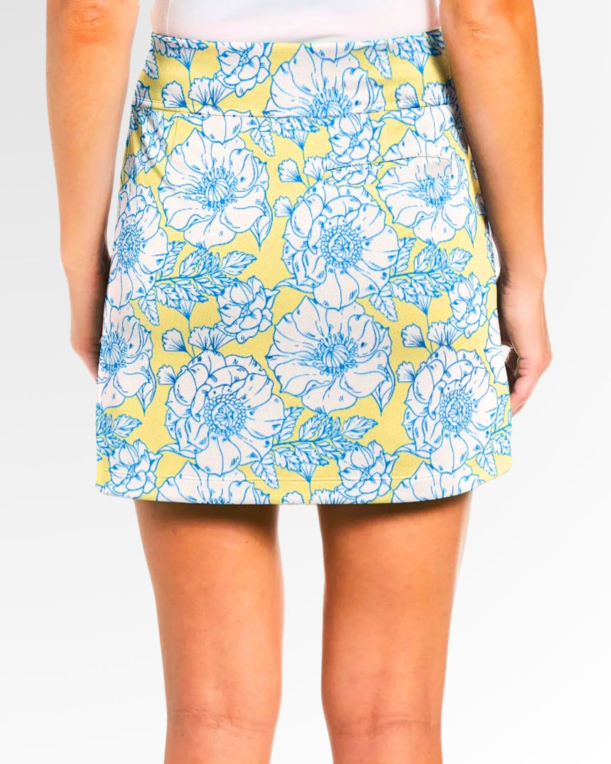 Close-up rear view of a woman wearing a yellow golf skort with a blue and white floral pattern.