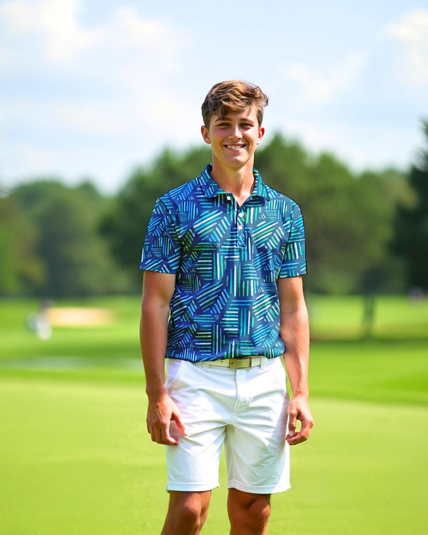 A smiling young man stands on a golf course wearing a patterned golf polo and white shorts.