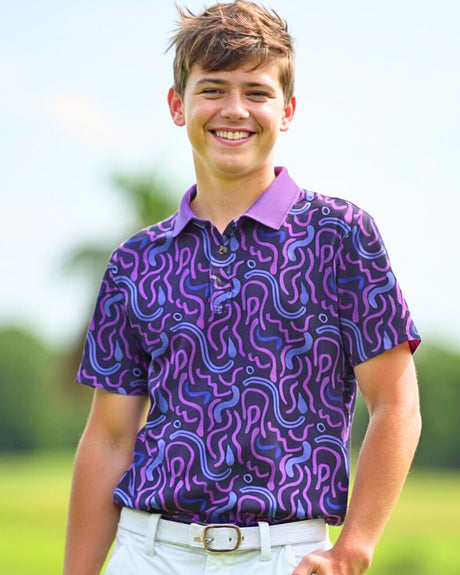 A smiling young man wearing a purple golf polo with a unique pattern, white pants, and a white belt.