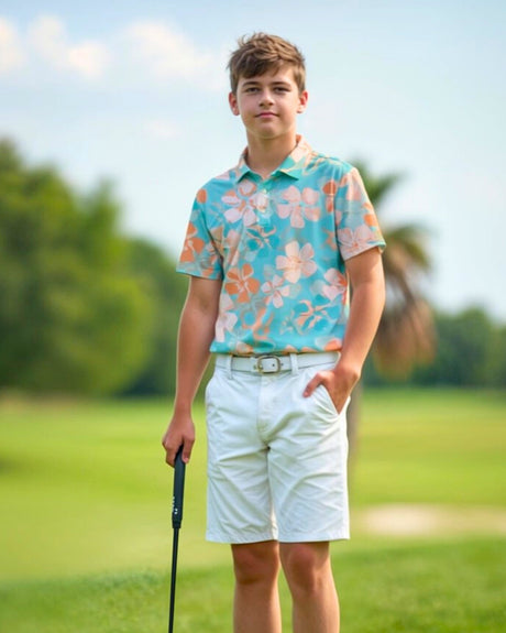 A young man stands on a golf course, wearing a floral golf polo, white shorts, and a white belt, holding a golf club.