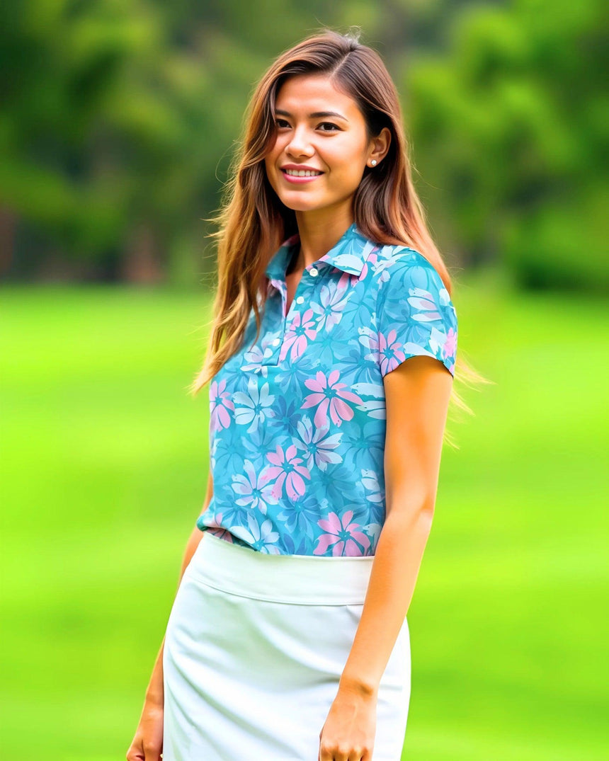 Woman wearing a blue floral golf polo and white pants standing on a grassy field.