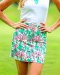 Person wearing a white top and colorful floral golf skirt on a green background
