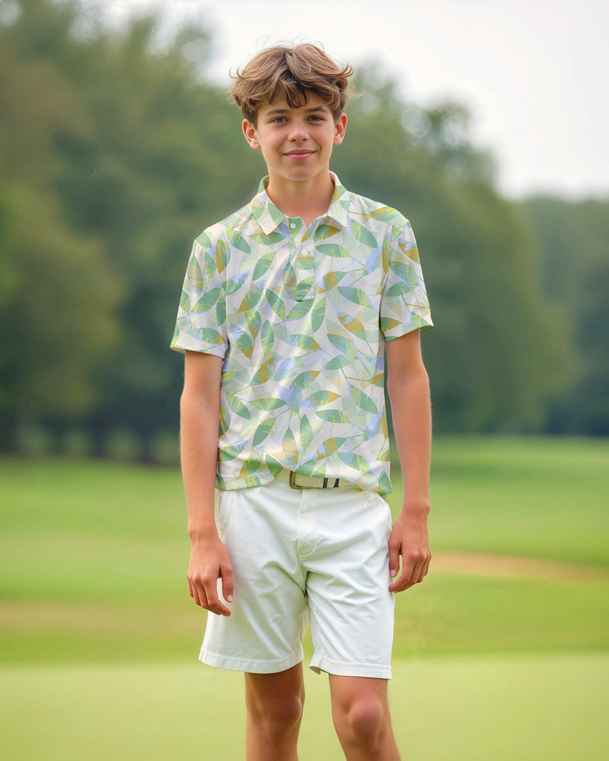 Young boy in a leaf floral print short sleeve polo and white shorts standing on a grassy field.
