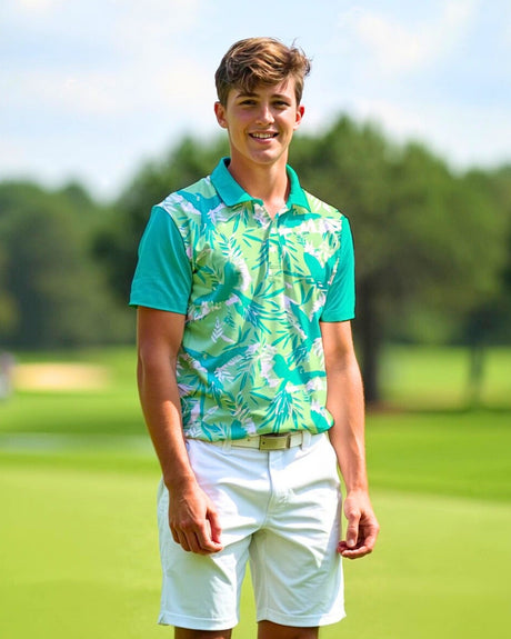 A smiling young man stands on a golf course wearing a green and white patterned golf polo, white shorts, and a white belt.