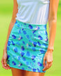 Close-up of a woman wearing a white golf polo and a turquoise golf skirt with a blue abstract pattern.