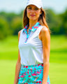 A woman wearing a white sleeveless golf polo with a flamingo print collar and matching flamingo print skirt stands on a golf course.