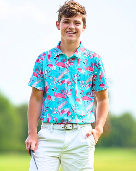 A young golfer smiles wearing a turquoise flamingo print polo shirt, white shorts, and a white belt.