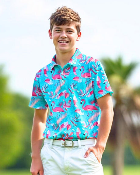 A young man smiles wearing a turquoise golf polo with a flamingo and tropical leaf pattern, paired with white pants and a white belt.