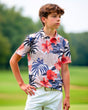 A young boy models a floral golf polo and white shorts on a golf course.
