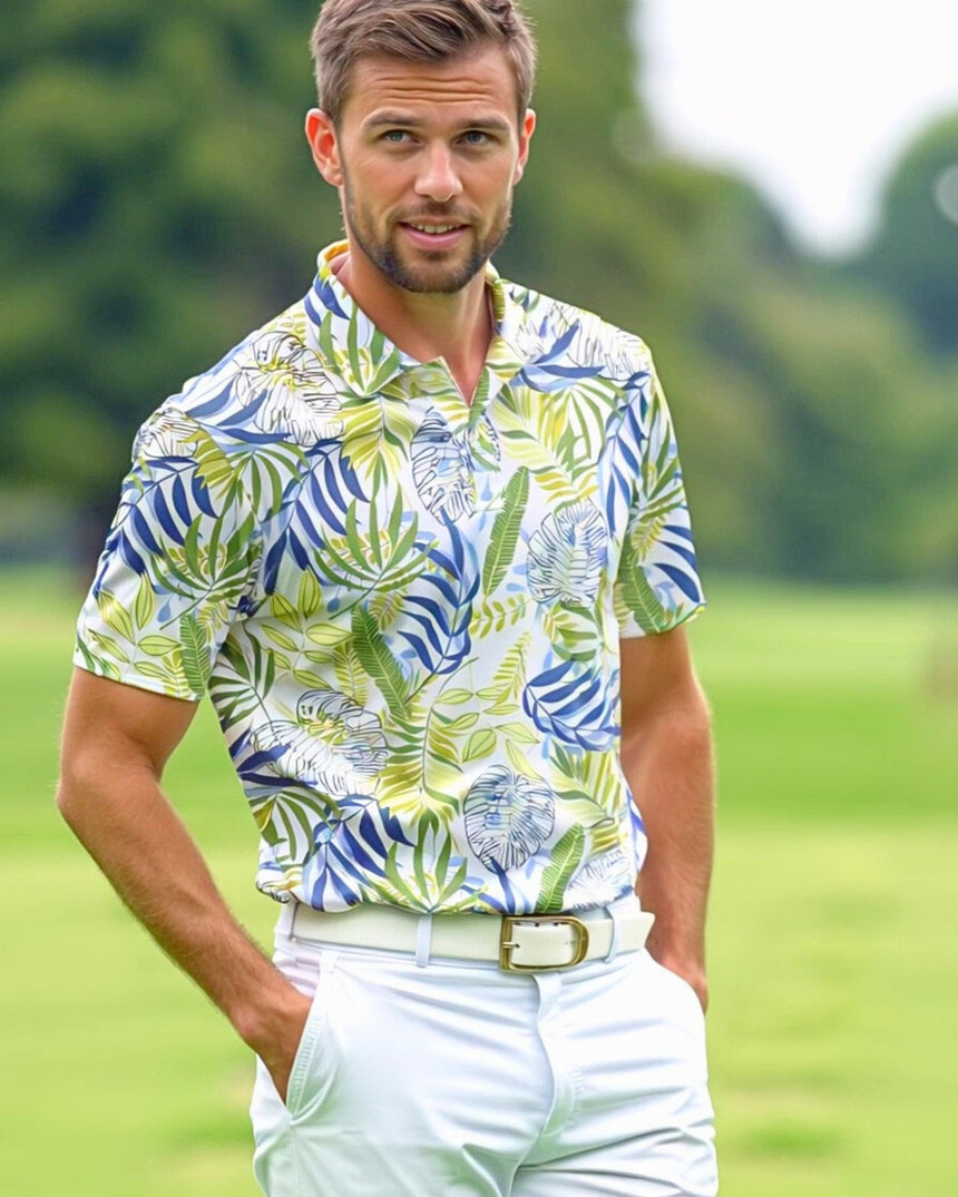 A man wearing a golf polo with a tropical leaf pattern, white pants, and a white belt stands on a golf course.