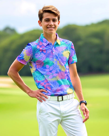 A smiling young man in a colorful tropical print golf polo, white pants, and a white belt stands on a golf course.
