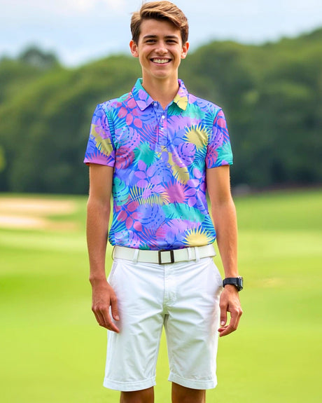 A smiling young man stands on a golf course wearing a colorful floral golf polo, white shorts, and a white belt.
