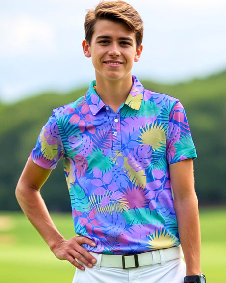 A young man smiles, wearing a colorful, tropical-patterned golf polo, white pants, and a white belt, standing on a golf course.