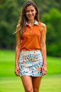 A woman smiles while wearing an orange sleeveless golf polo and a patterned golf skirt.