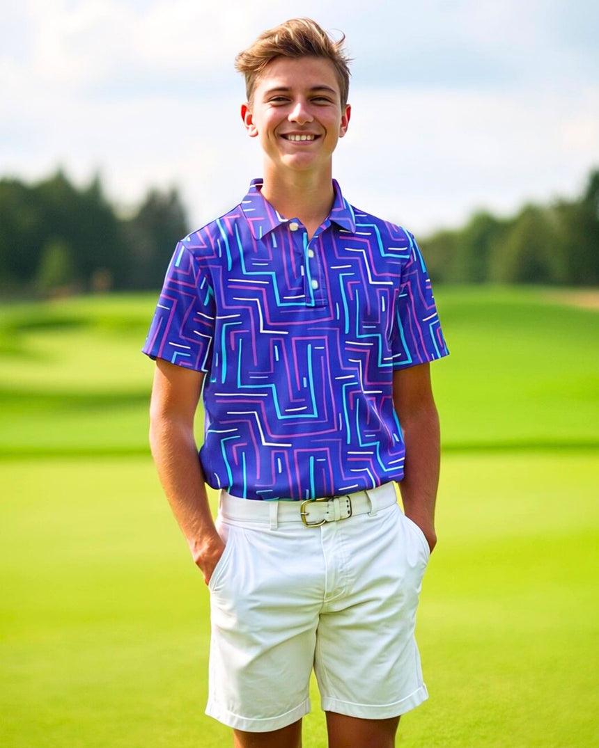 A young man smiles while wearing a purple golf polo with a geometric design, paired with white shorts and a belt, standing on a golf course.