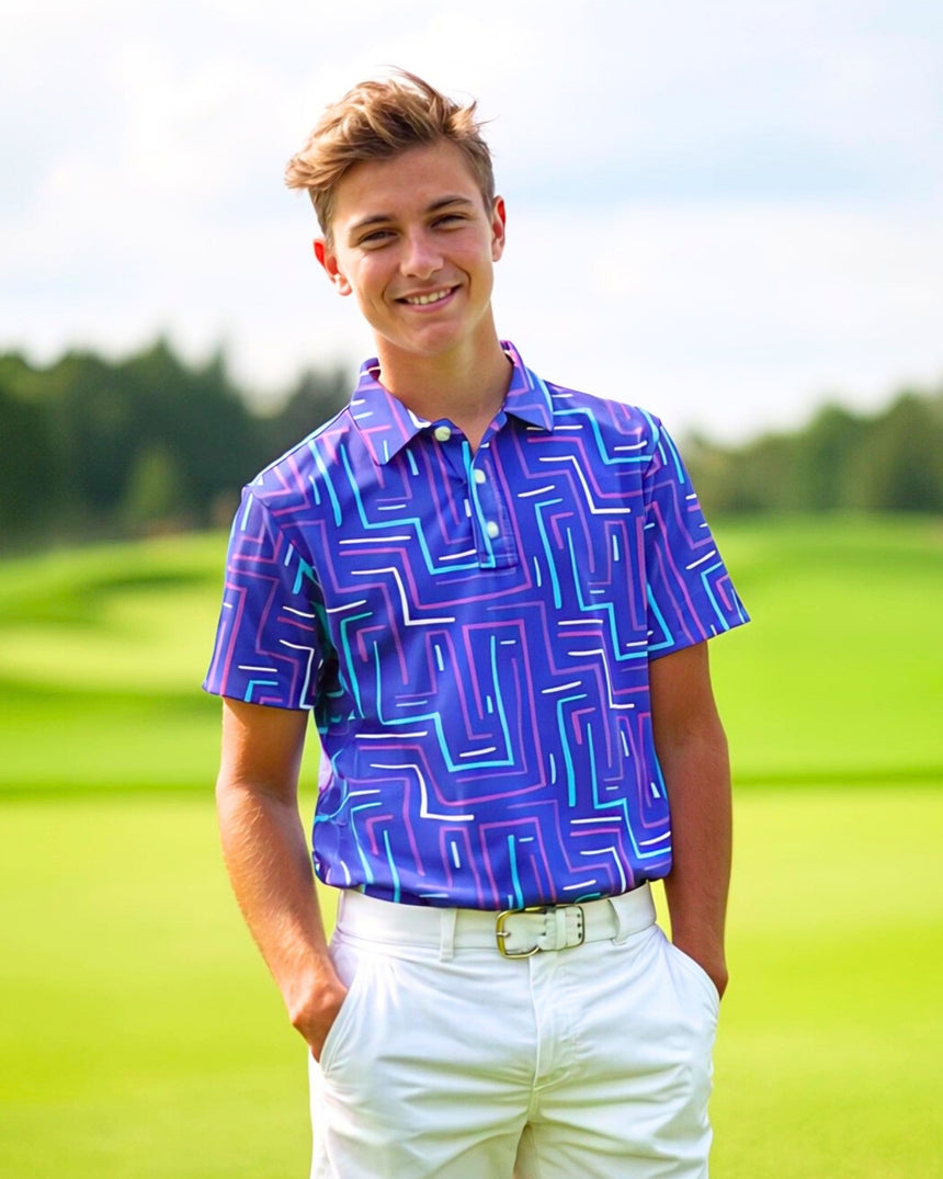 A young man smiles, wearing a patterned golf polo and white pants on a golf course.