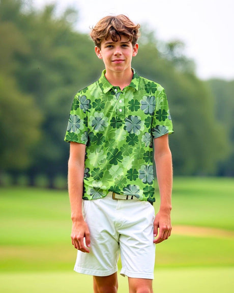 A young man stands on a golf course wearing a green golf polo with a clover pattern and white shorts.