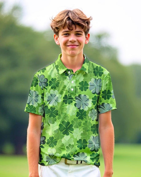 A smiling young man stands on a golf course wearing a green golf polo with a clover pattern.