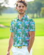 A man on a golf course wearing a tropical pink and green print golf polo shirt