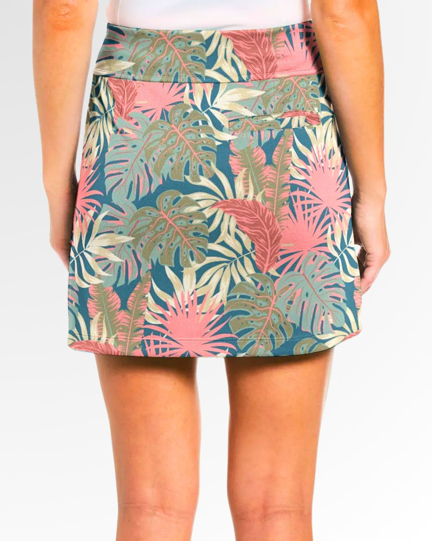 Close-up back view of a woman wearing a golf skort with a tropical leaf pattern in pink, green, and beige on a blue background.