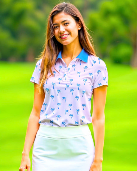 A smiling woman in a golf polo with a palm tree pattern and a white skirt stands on a golf course.